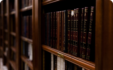 Close-up view of a dark wooden bookshelf filled with a row of uniform, dark red books with gold lettering, suggesting a specialized library collection.