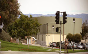A large, cylindrical green water storage tank and a smaller utility building sit on a grassy hill, visible behind a traffic light pole and a small parking lot.